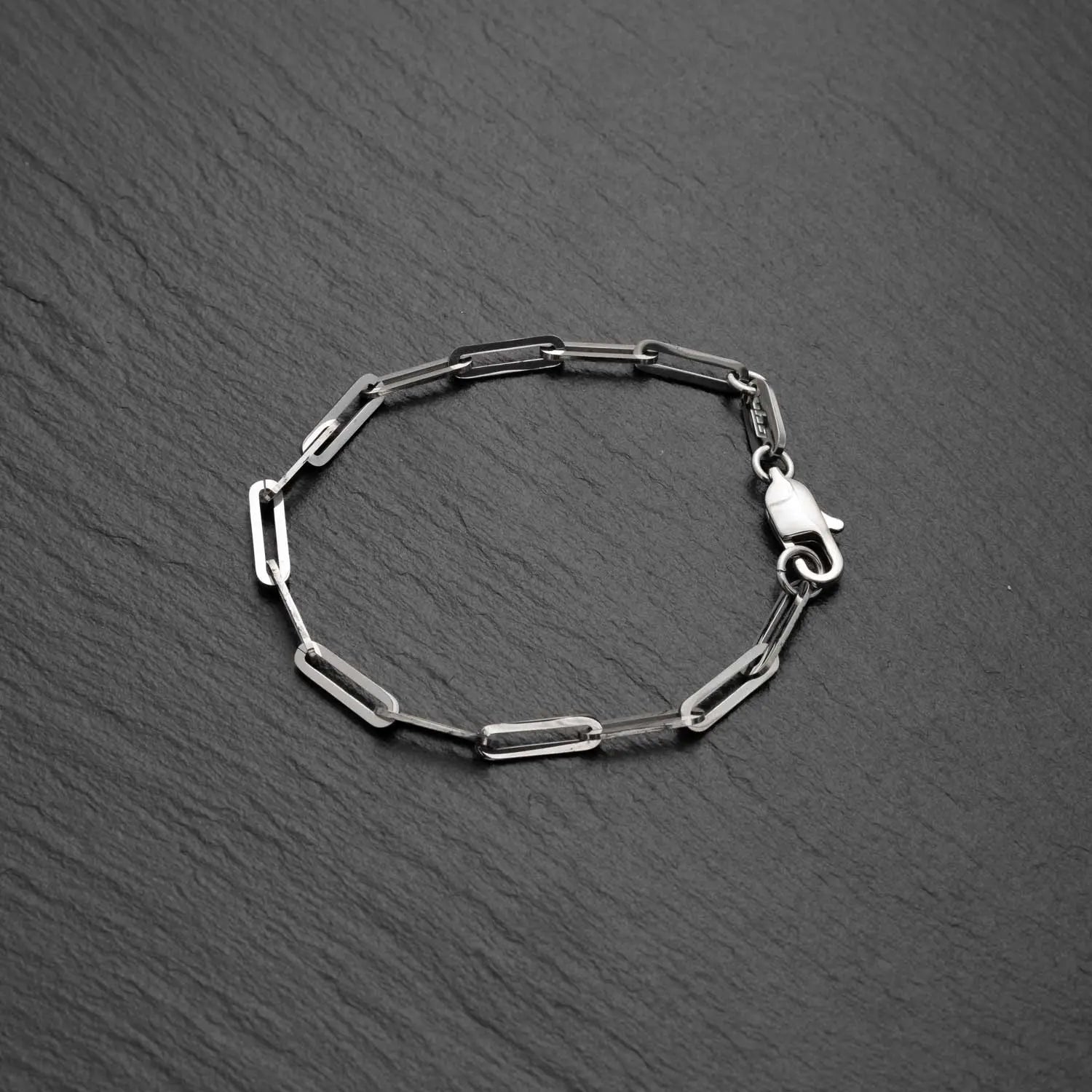 Herren Paperclip Armband aus Edelstahl mit Gliedern in Büroklammerform auf einem rauen schwarzen Hintergrund